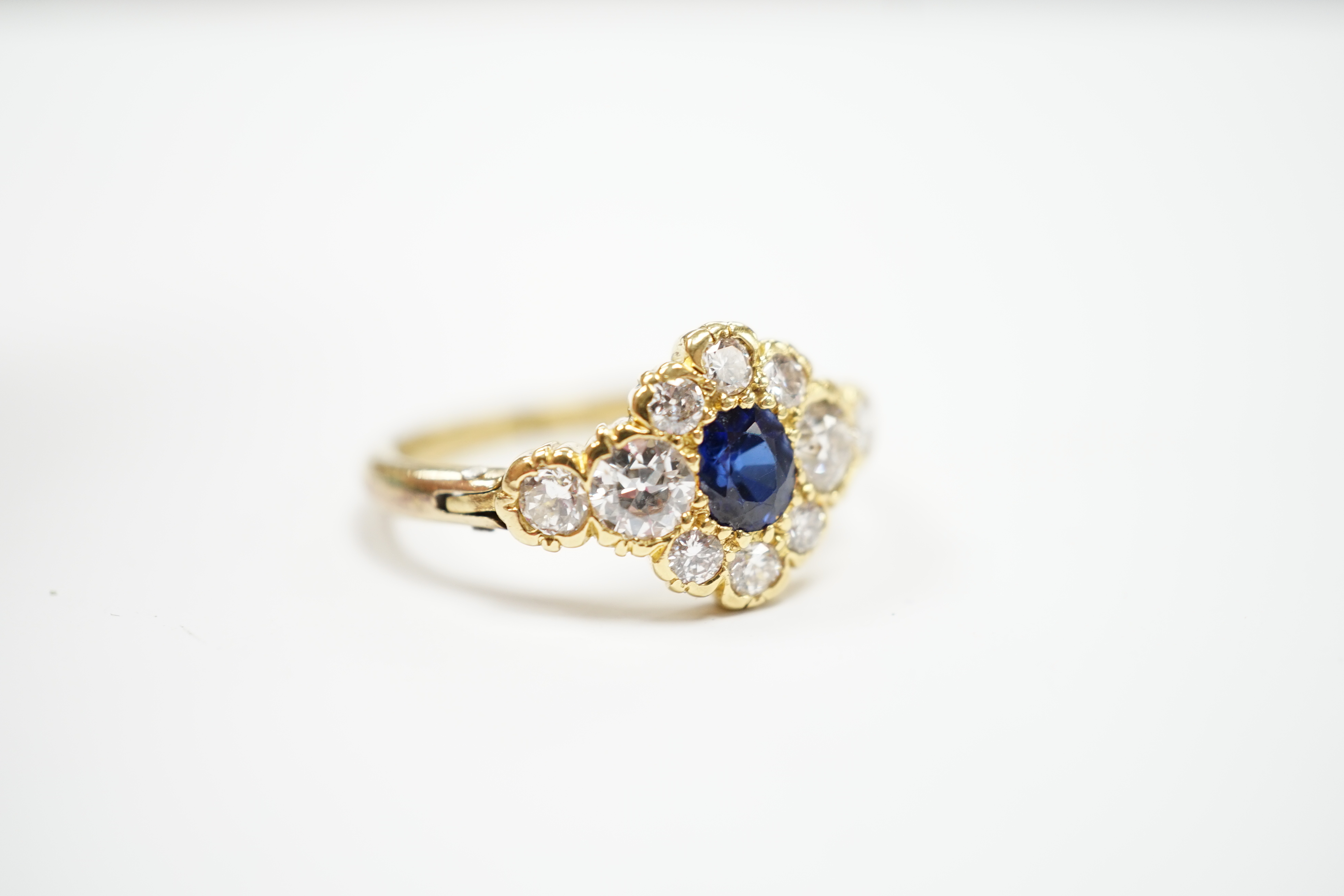 A modern yellow metal, synthetic sapphire and diamond set flower head cluster ring, with hinged shank, size U, gross weight 5.1 grams.